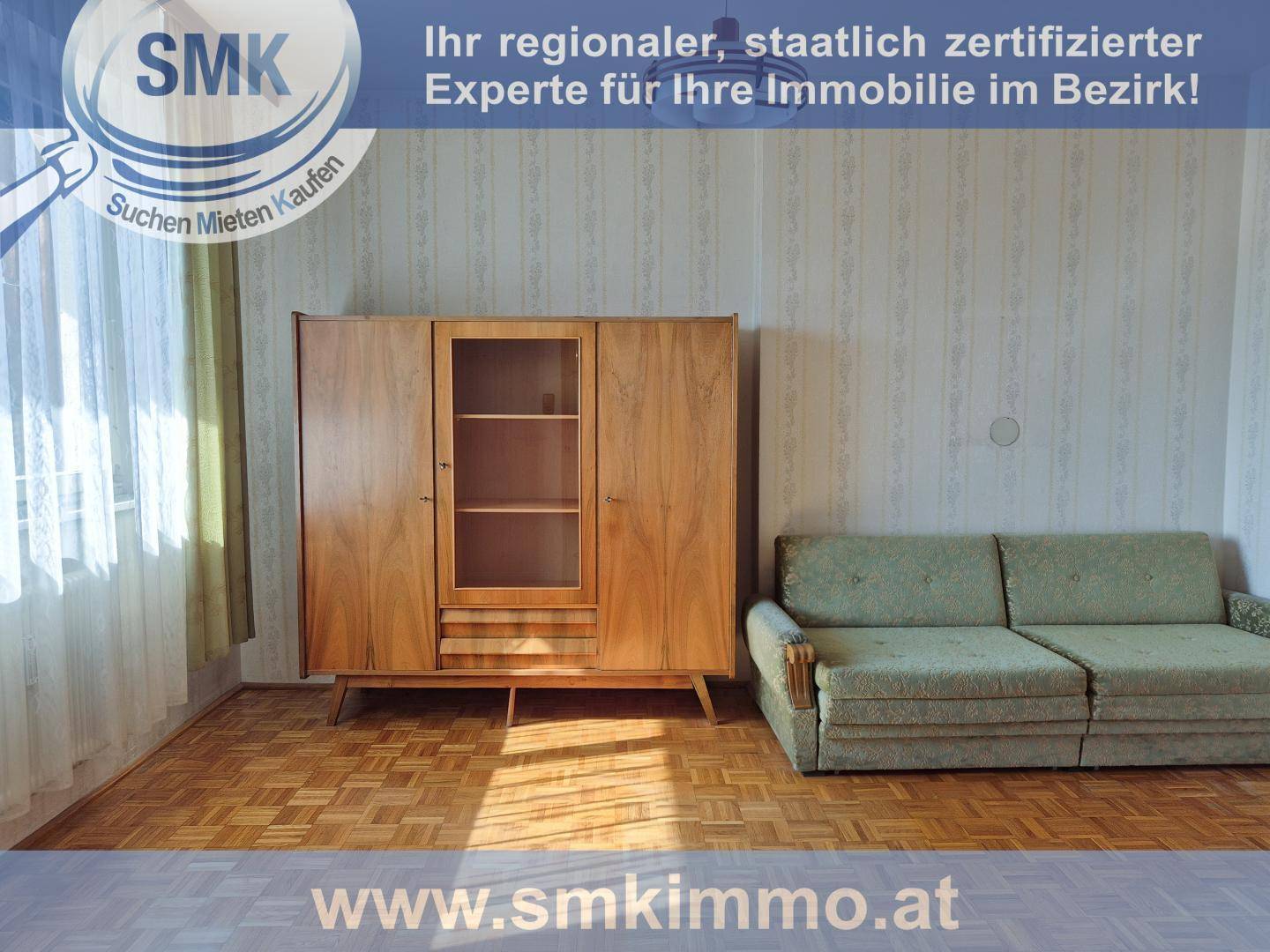 Wohnzimmer mit Fischgrätparkett, einem Vintage-Schrank und einem älteren Sofa in einem hellen Raum.