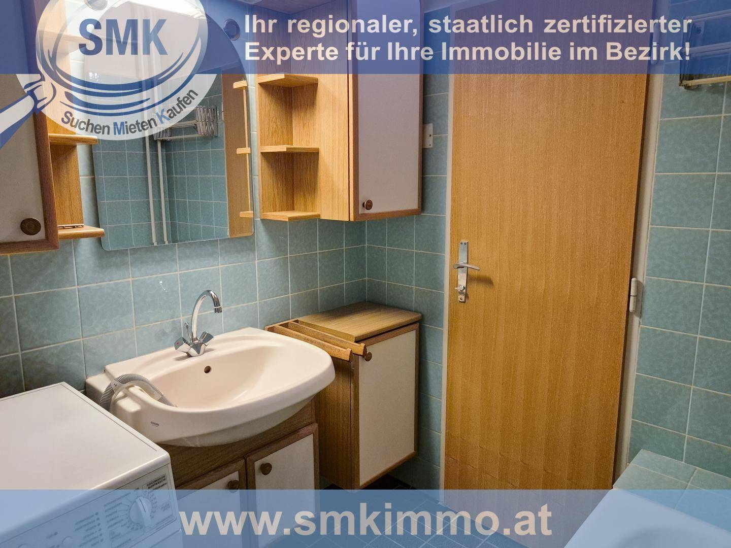 Badezimmer mit hellblauen Fliesen, einem Waschbecken, Spiegel und einer Waschmaschine.