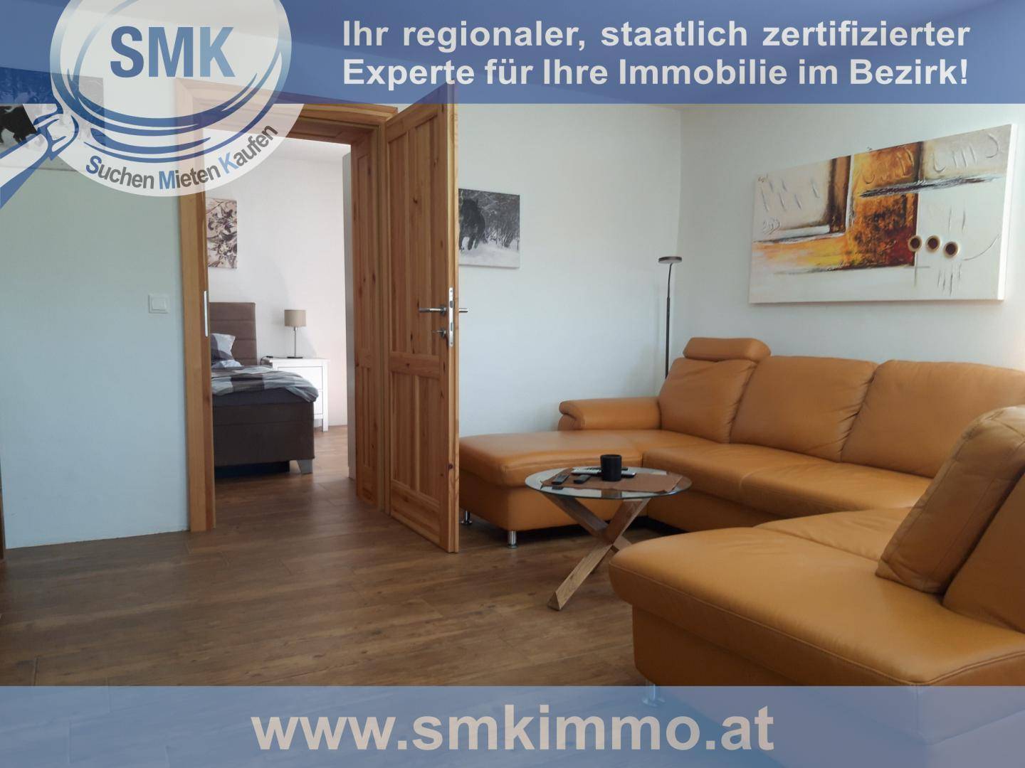 Gemütliches Wohnzimmer mit großer Ledercouch, Holzboden und Zugang zum Schlafzimmer.