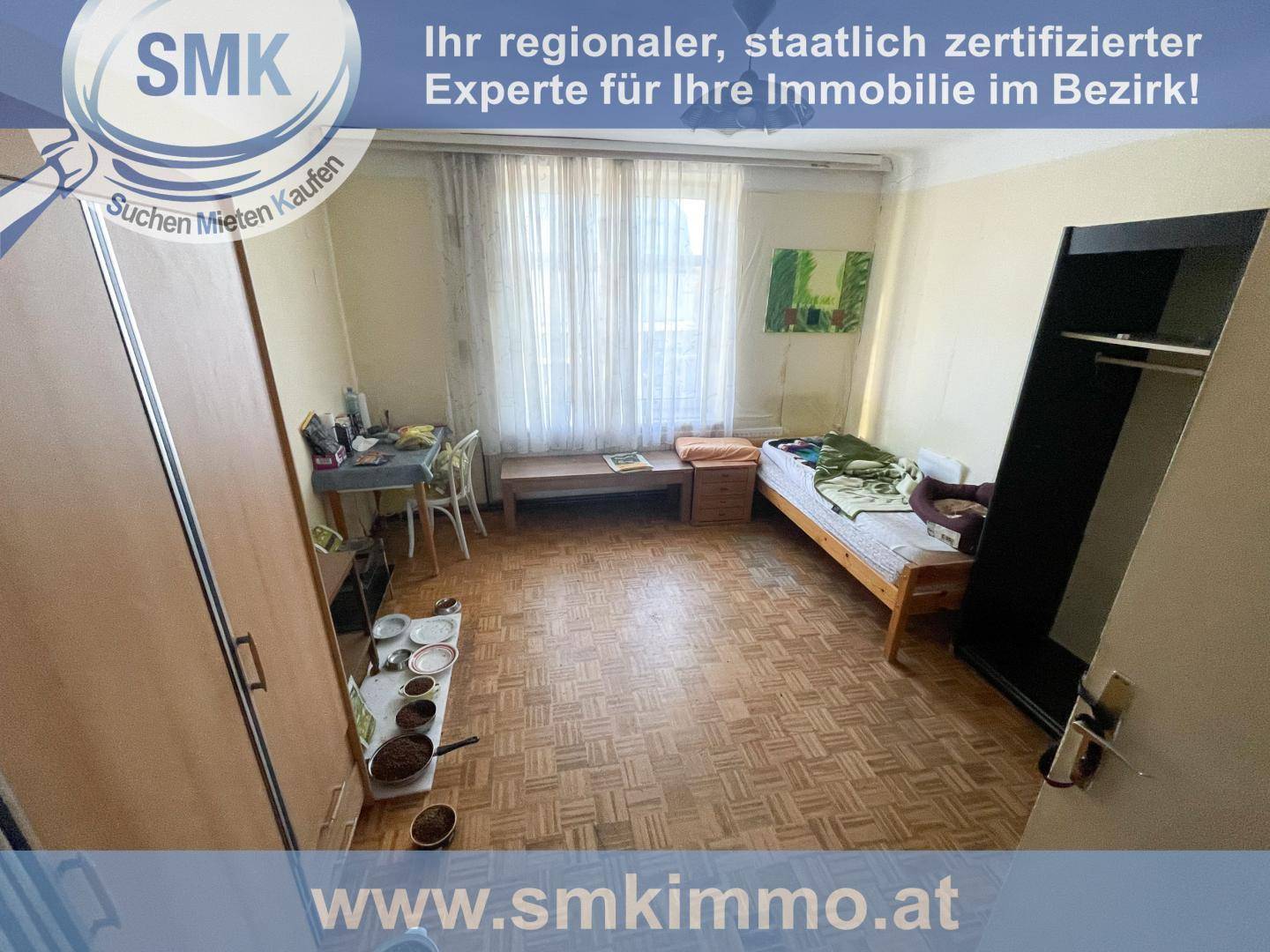 Schlafzimmer mit altem Parkettboden, Einzelbett, Kleiderschrank und Schreibtisch am Fenster.