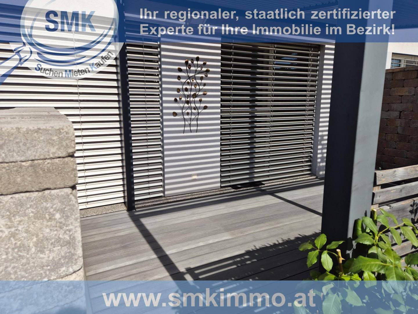 Terrassenbereich mit Holzdielen, einem Steinpfeiler und geschlossenen Fensterläden am Haus.