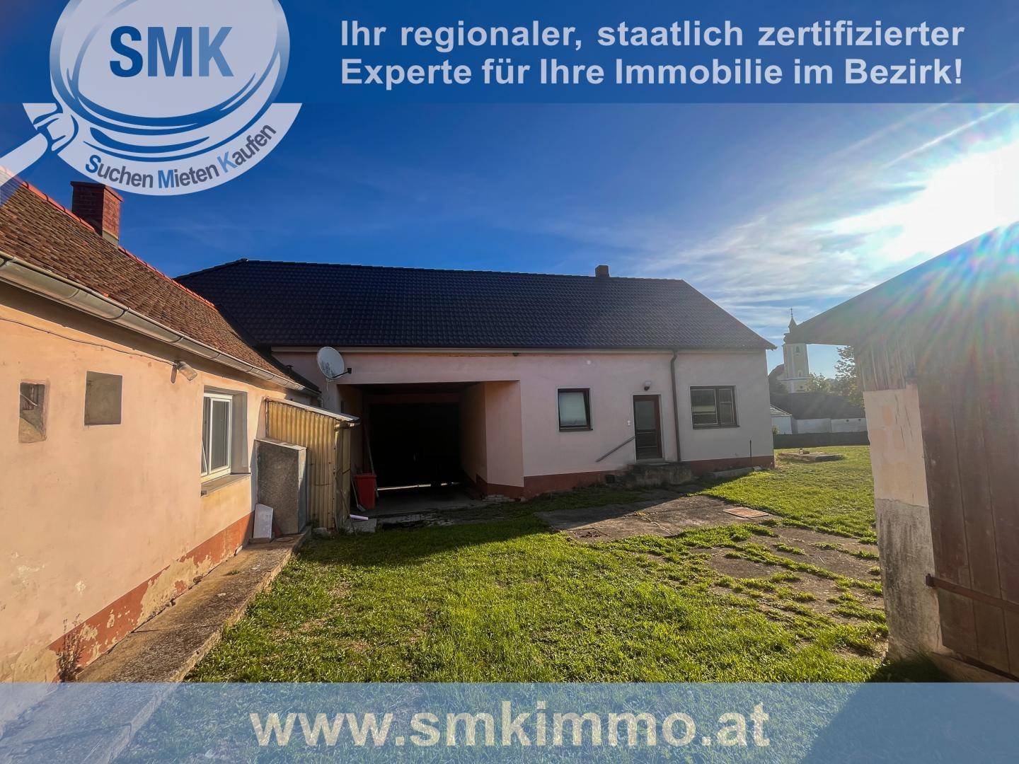 Rückansicht des Gebäudes mit großem Gartenbereich und angrenzendem Nebengebäude unter strahlend blauem Himmel.