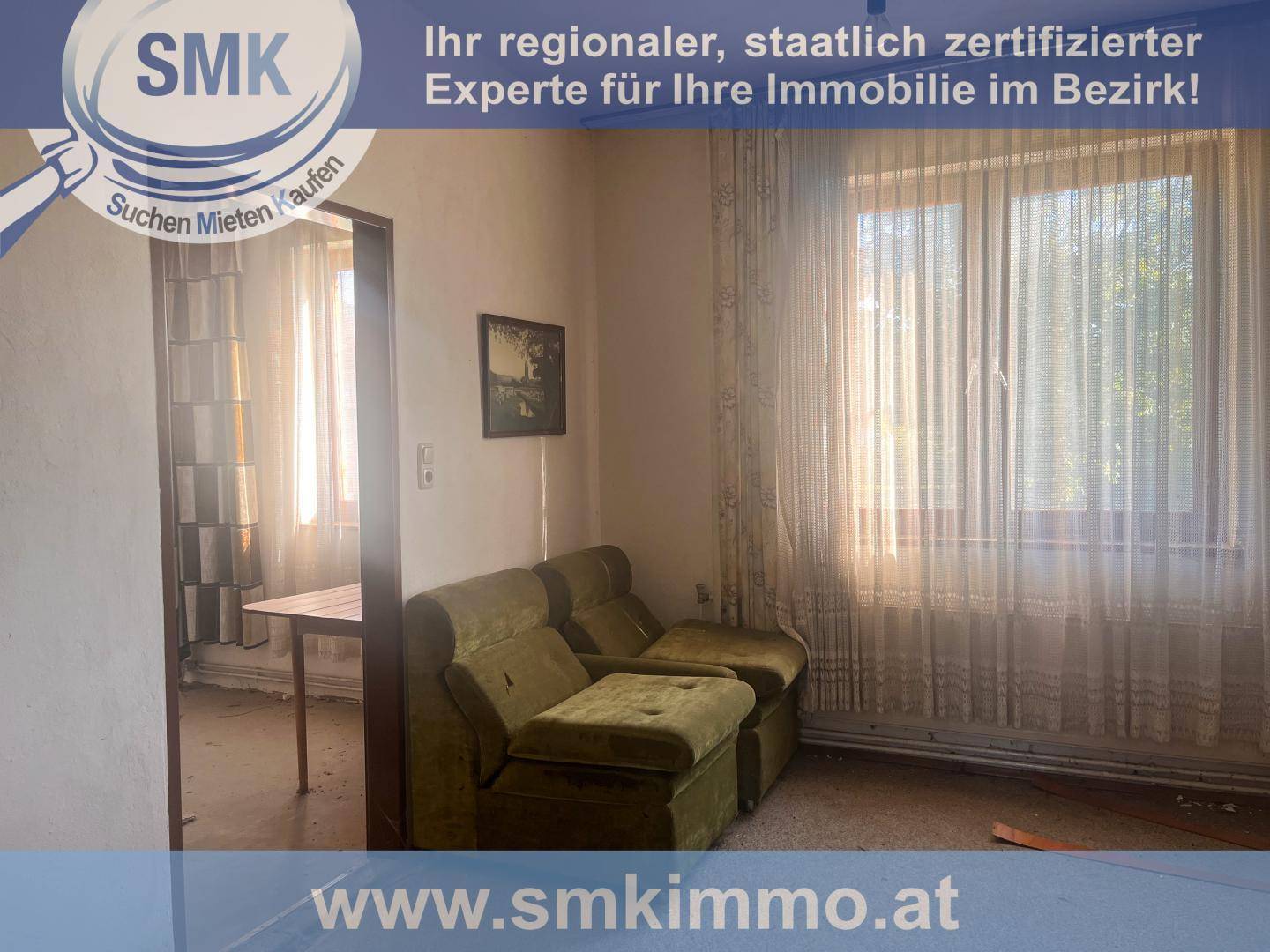 Wohnzimmer mit grünen Polstermöbeln, einem Tisch und einem großen Fenster mit Vorhängen.