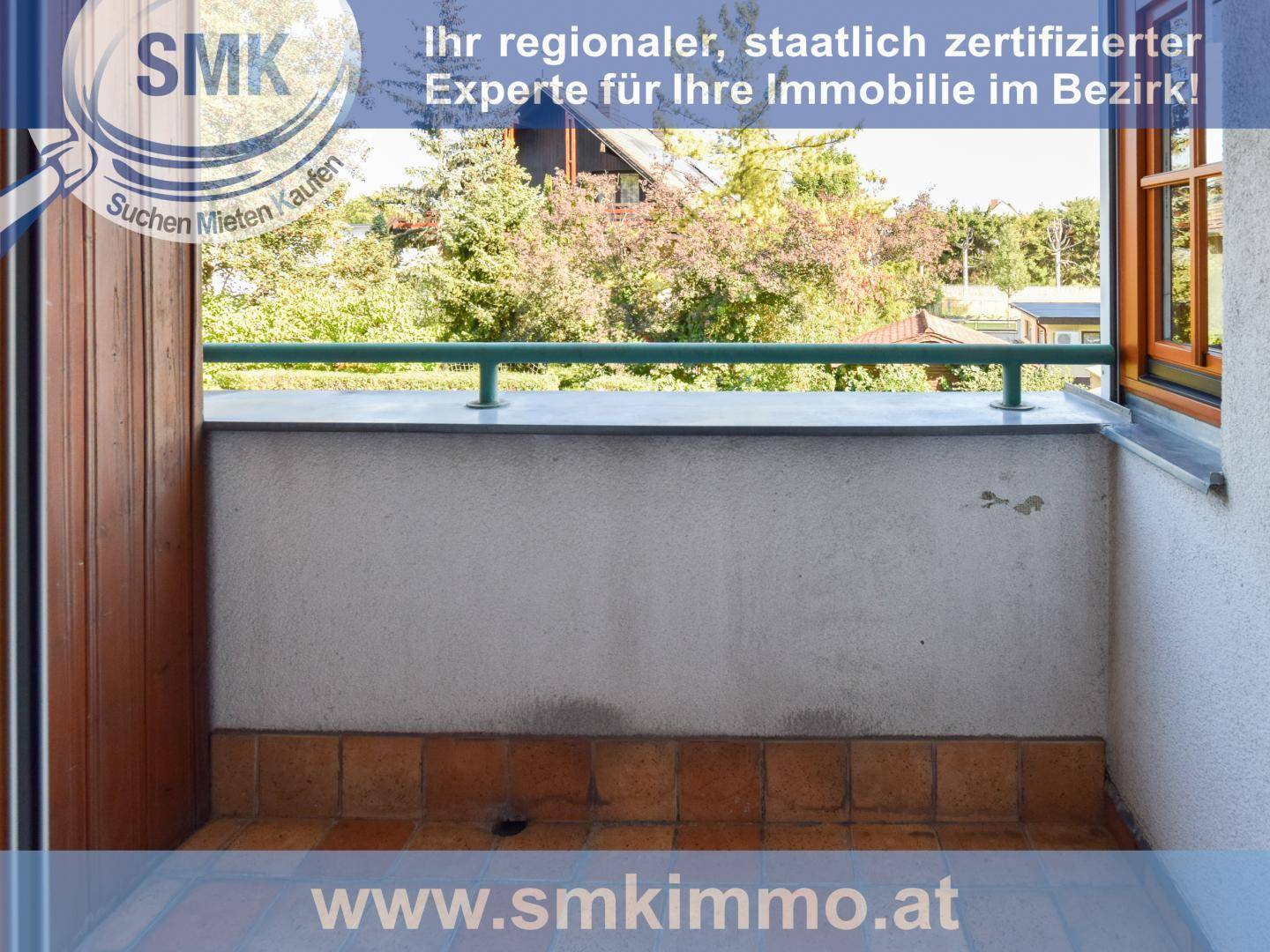 Kleiner Balkon mit Fliesenboden und Blick auf grüne Bäume.