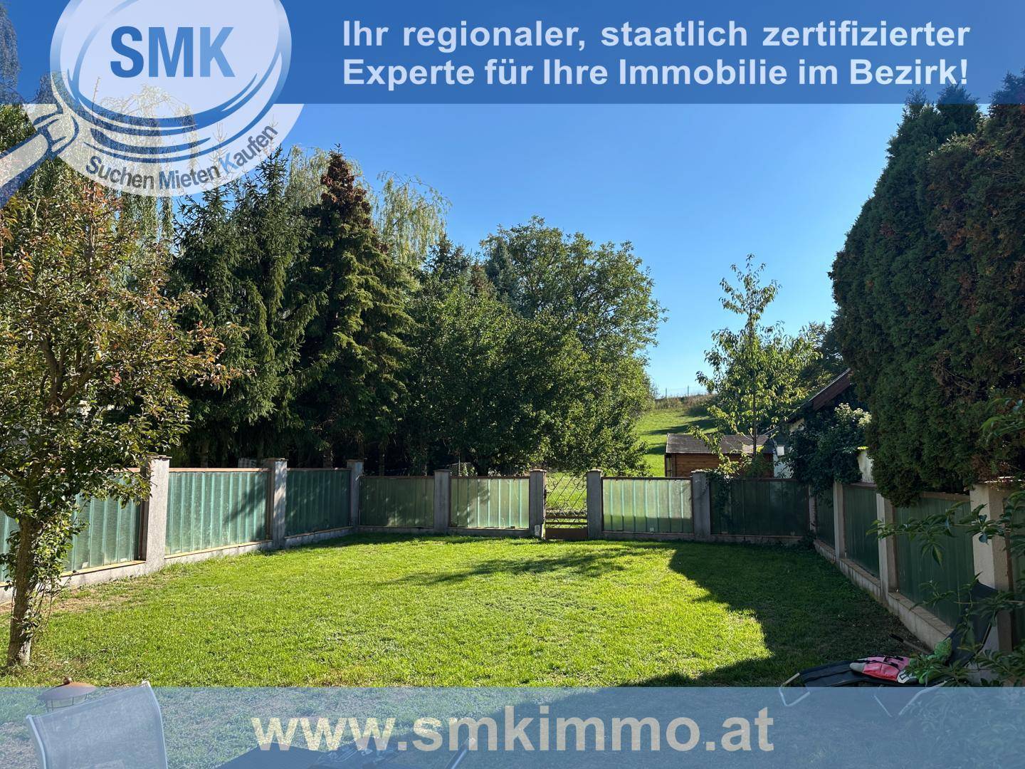 Weitläufiger Garten mit Rasenfläche, umzäunt und umgeben von hohen Bäumen.