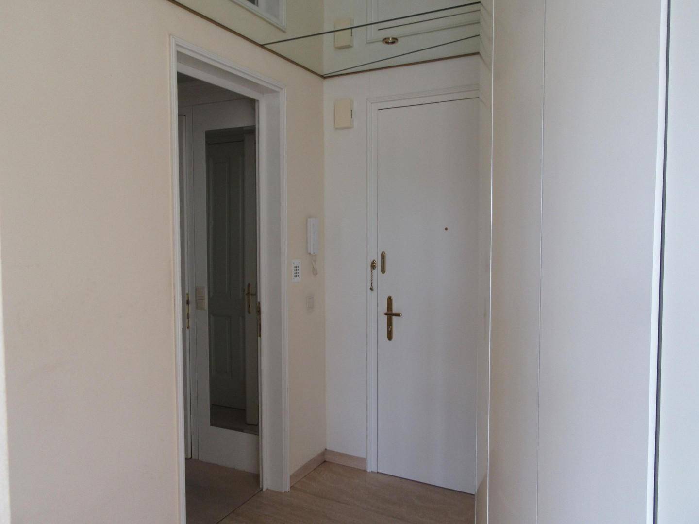 Eingangsbereich mit heller Tür, Spiegelfliesendecke und Zugang zu weiteren Räumen.