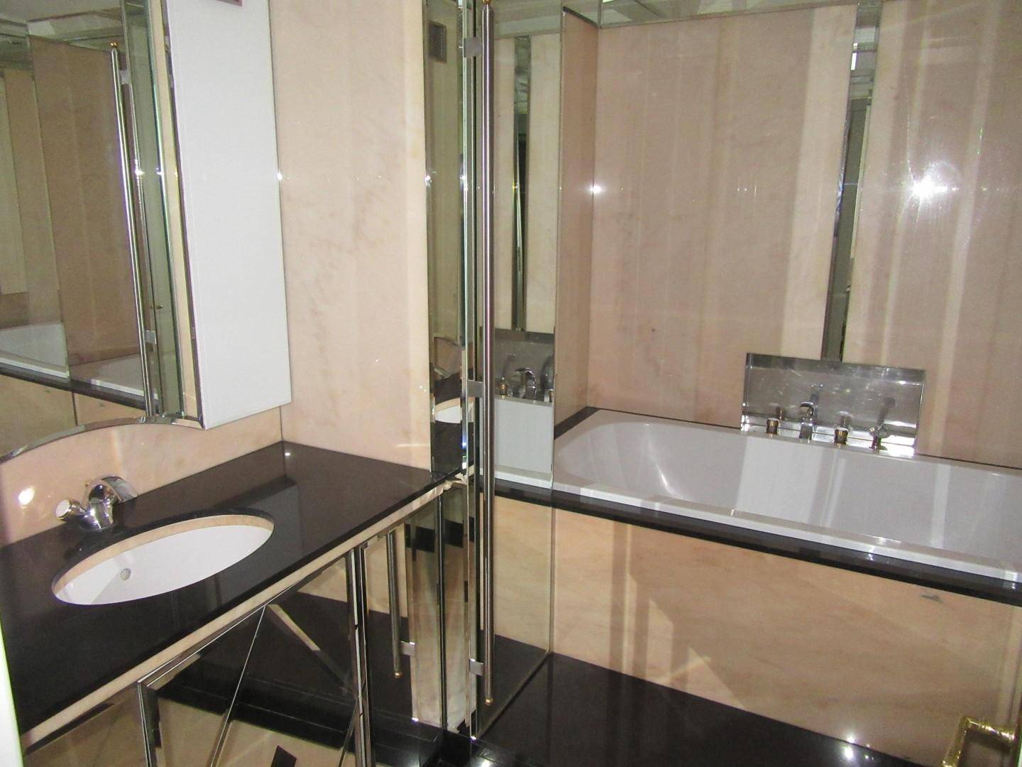Elegantes Badezimmer mit Badewanne, schwarzer Arbeitsplatte und verspiegelten Wänden.