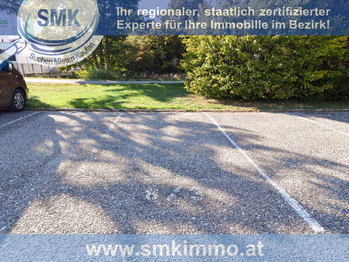 Außenparkplätze mit Schotterbelag und Bäumen im Hintergrund, bieten Stellflächen für Fahrzeuge.