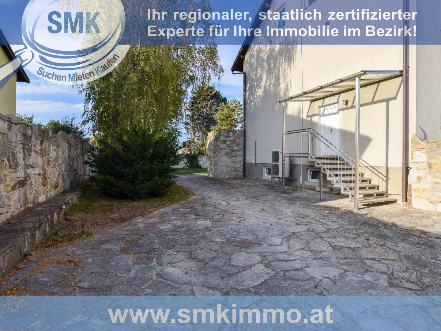 Seitenansicht des Hauses mit gepflasterter Auffahrt und Außentreppe zum Eingang.