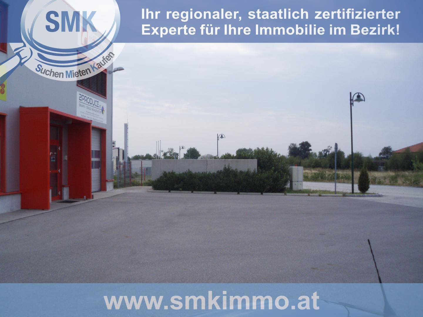 Außenbereich eines Geschäftsgebäudes mit großem Parkplatz und rotem Eingangsbereich unter bewölktem Himmel.