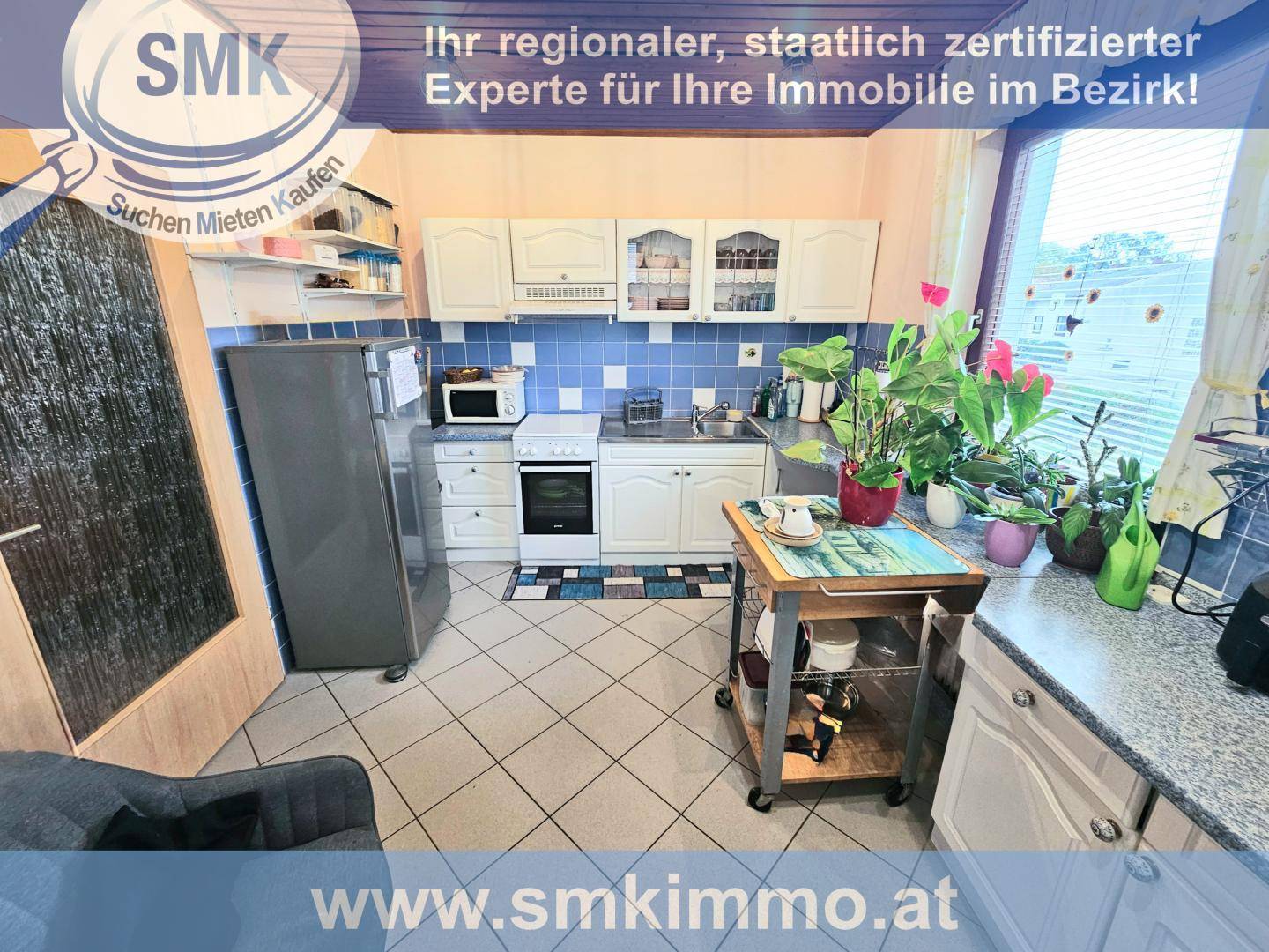 Funktionale Küche mit weißen Schränken, blau-weiß gefliestem Spritzschutz und Fenster.