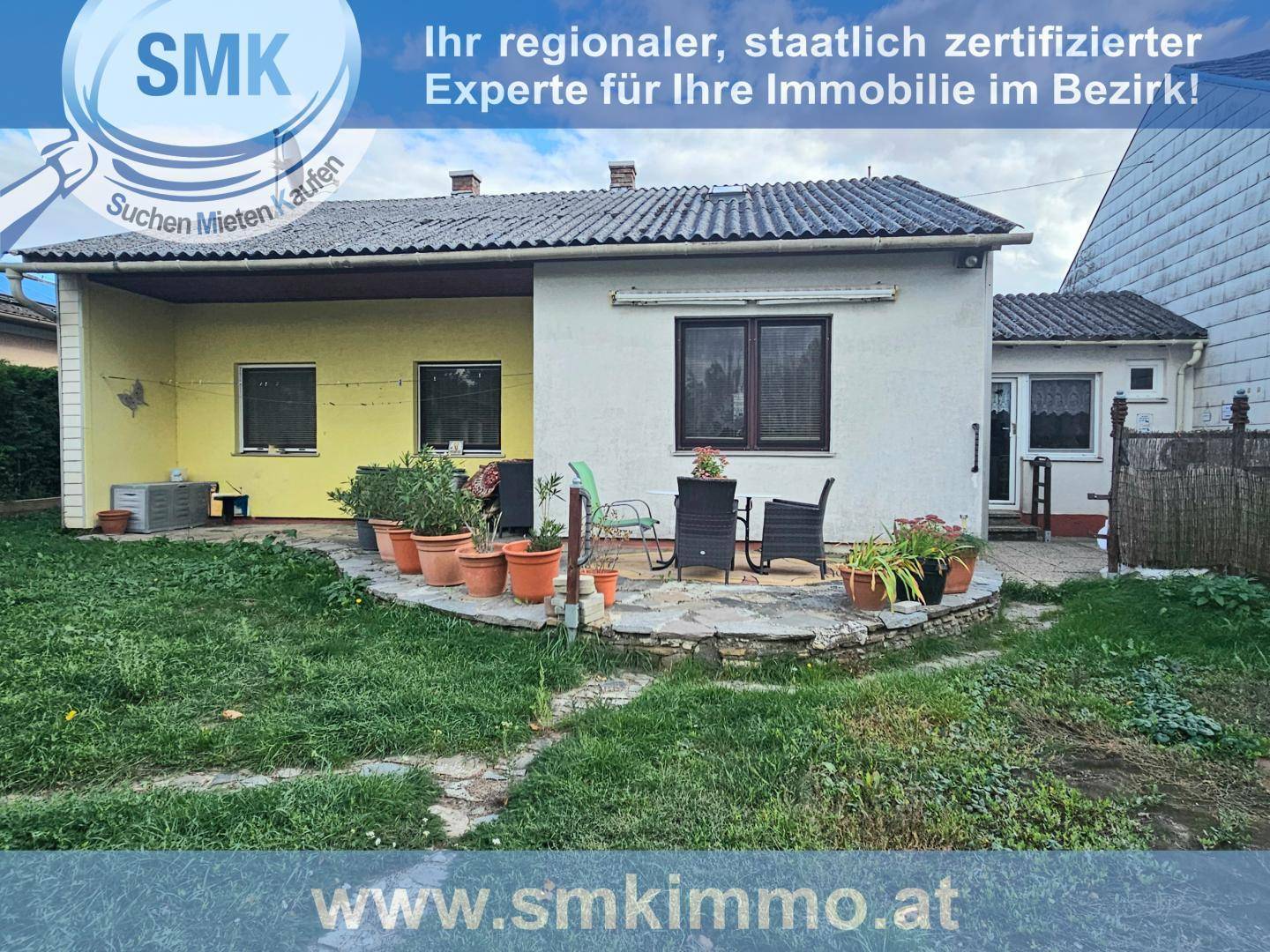 Rückseite des Hauses mit kleiner Terrasse, Gartenmöbeln und angrenzender Grünfläche.