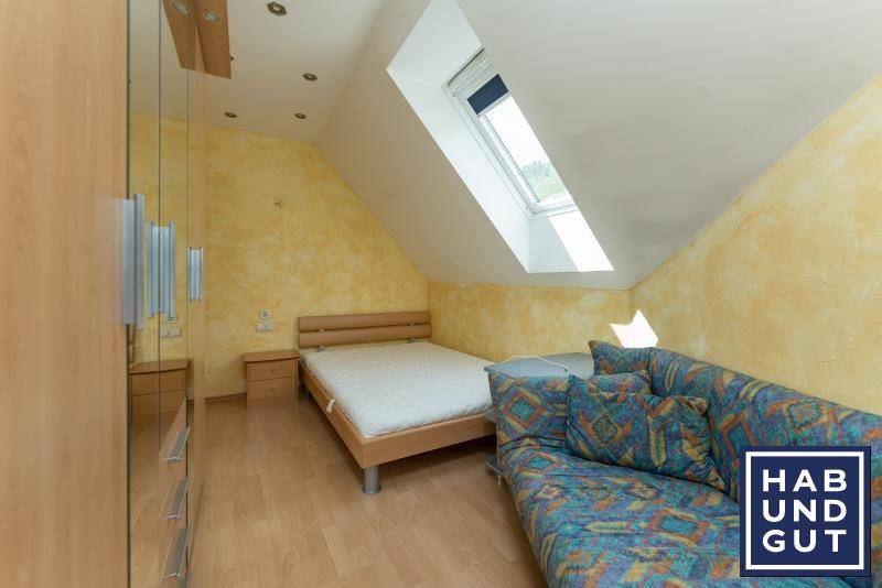 Gemütliches Schlafzimmer im Dachgeschoss mit Bett, Sofa und Dachfenster.