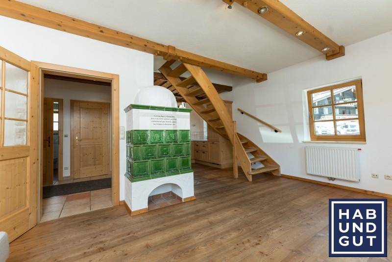 Wohnbereich mit traditionellem Kachelofen, Holztreppe und sichtbaren Deckenbalken.