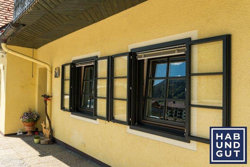 Nahaufnahme der gelben Fassade mit geöffneten Fenstern und traditionellen schwarzen Fensterläden.