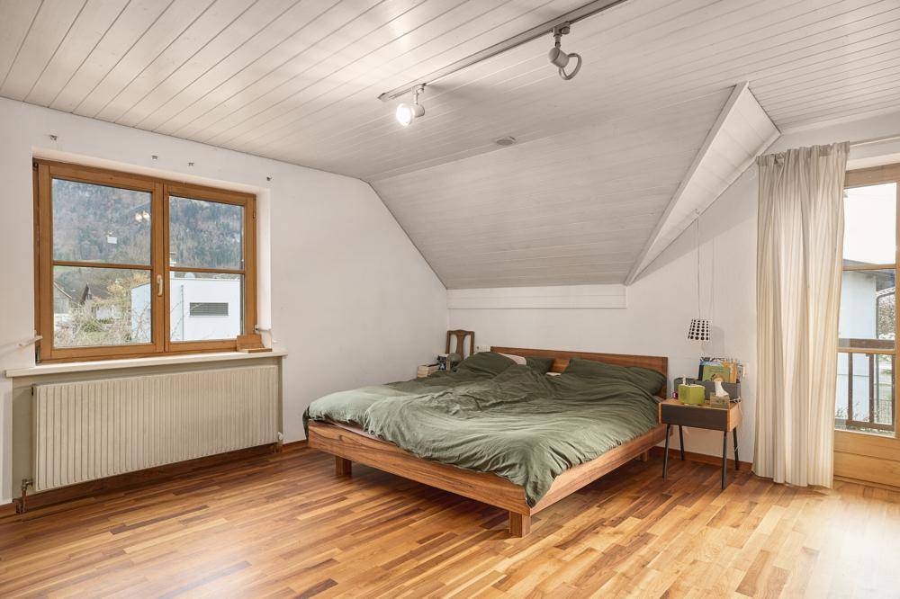 Schlafzimmer mit Holzboden, Dachschräge und Zugang zu einem kleinen Balkon.