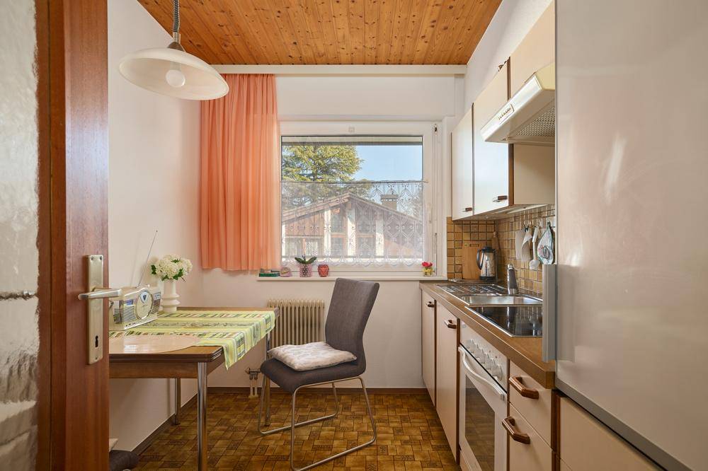 Funktionale Küche mit Holzbalkendecke, Essbereich und Blick ins Grüne durch das Fenster.