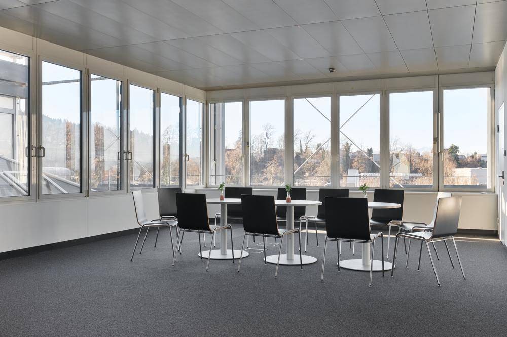 Heller Besprechungsraum mit runden Tischen, modernen Stühlen und weitem Ausblick durch die Fensterfront.