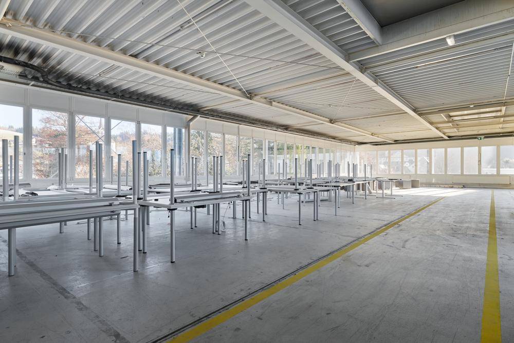 Große Halle mit vielen Tischen, hohen Decken und Betonboden, ideal für Produktion oder Lagerung.