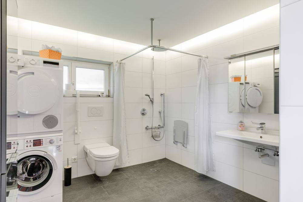 Modernes Badezimmer mit ebenerdiger Dusche, Waschmaschine, Trockner und Wand-WC.