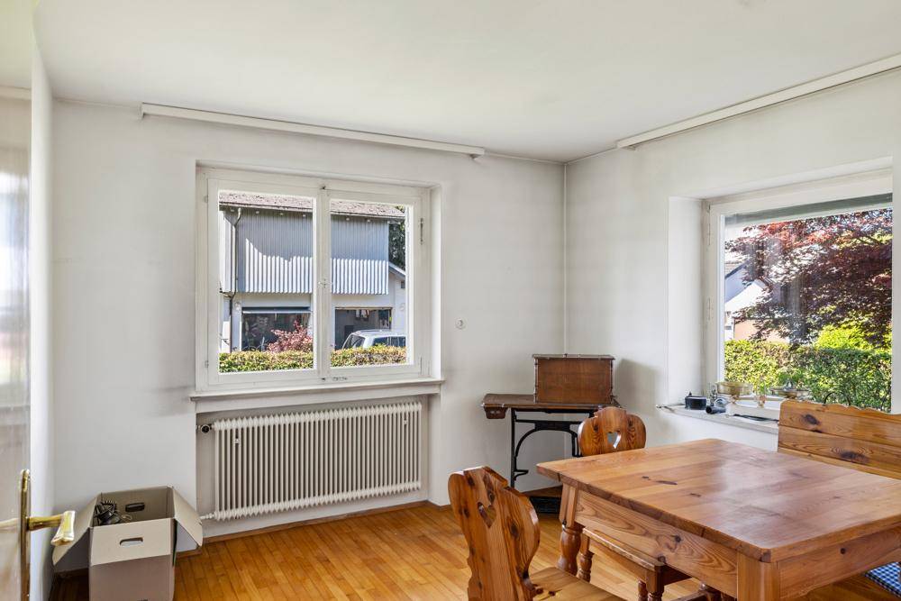 Esszimmer mit rustikalem Holztisch, Stühlen und Blick ins Grüne durch die Fenster.