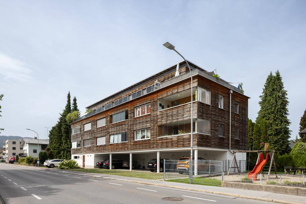 Modernes Mehrfamilienhaus mit Holzfassade, Balkonen und Spielplatz in der Umgebung.