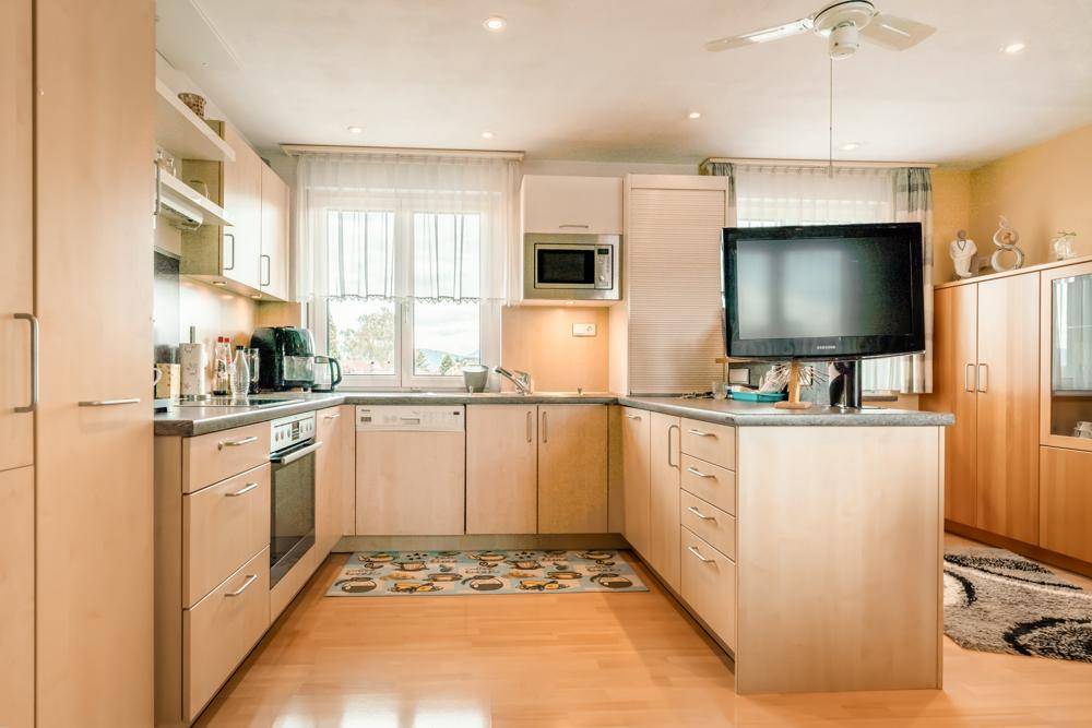 Helle Einbauküche mit Holzfronten, modernen Geräten und Deckenventilator.