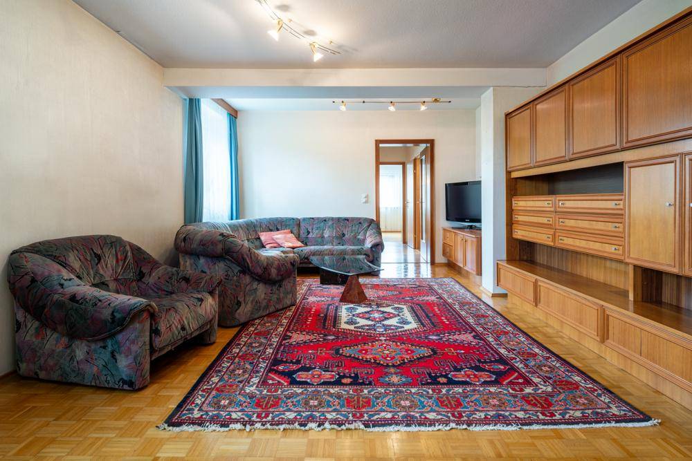 Gemütliches Wohnzimmer mit traditionellem Teppich, Holzmöbeln und Blick in den Flur.