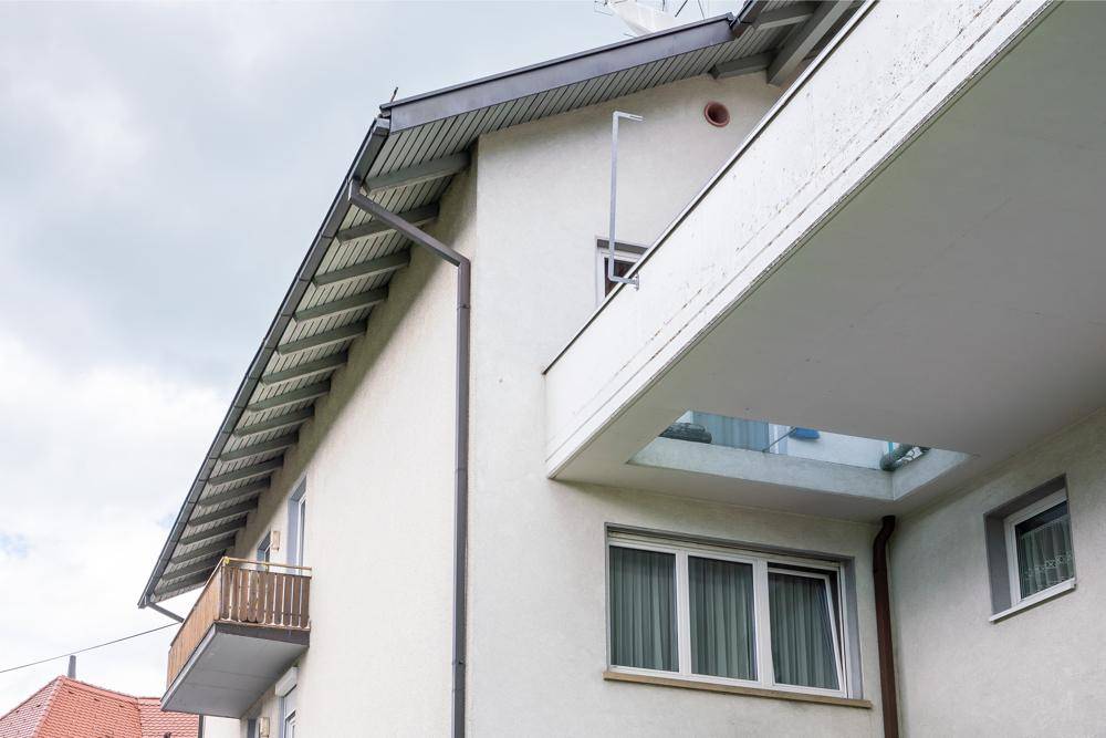 Detailansicht der Gebäudefassade mit Balkonen und Dachüberstand unter bewölktem Himmel.