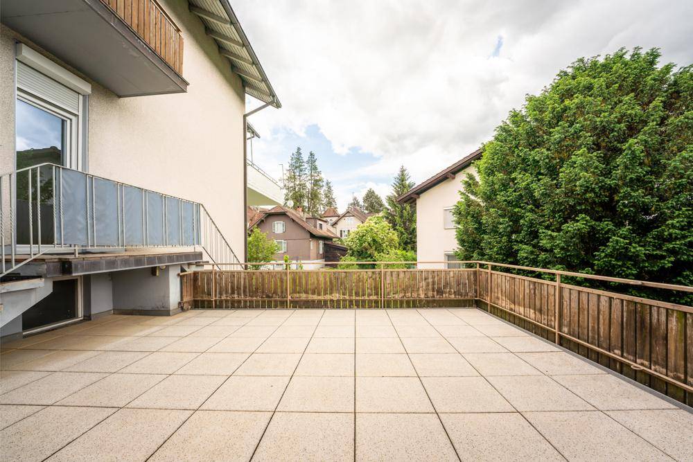 Große geflieste Terrasse mit Holzgeländer und Blick auf die Nachbarschaft.