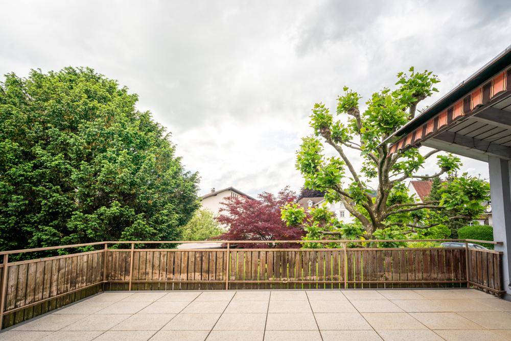 Weitläufige Terrasse mit Fliesenboden und Blick auf Bäume und umliegende Häuser.