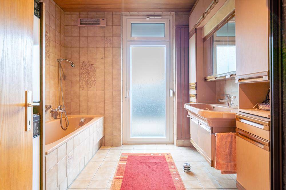 Badezimmer mit beiger Badewanne, Fliesenboden und Fenster.