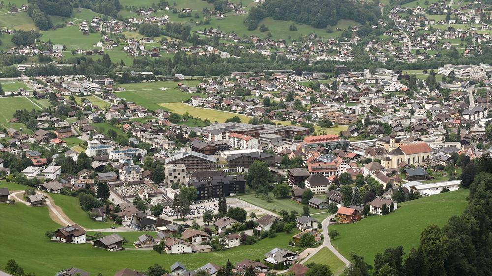 Weitläufige Luftaufnahme einer Stadt in einem Tal, umgeben von grünen Hügeln und verstreuten Häusern.