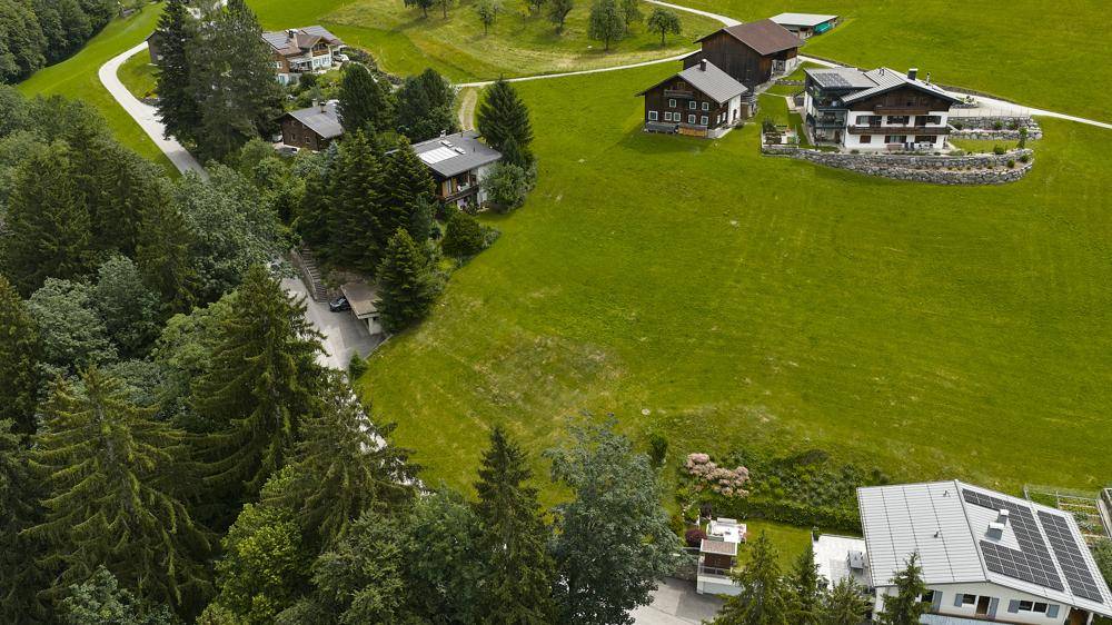 Luftaufnahme von Häusern in einer hügeligen, grünen Landschaft mit Bäumen und Straßen, einige mit Solaranlagen.