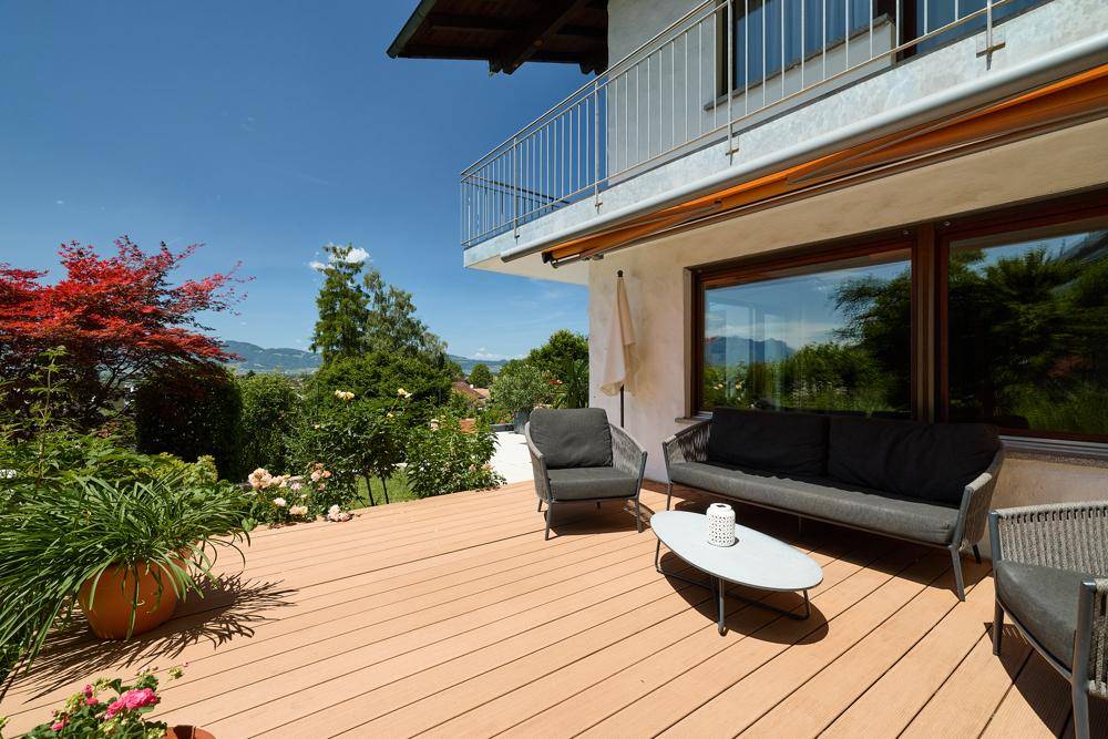 Sonnige Holzterrasse mit Lounge-Möbeln, Blick auf die Berge und das umliegende Grün.