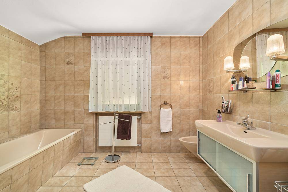 Badezimmer im 80er-Jahre-Stil mit beigefarbenen Fliesen, Badewanne und Fenster.