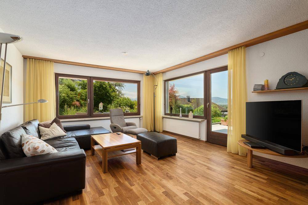 Geräumiges Wohnzimmer mit Holzboden, großen Fenstern und weitem Blick in die Landschaft.