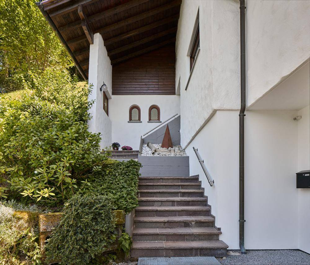 Eingangsbereich des Hauses mit Steintreppe, Handlauf und begrünten Mauern.