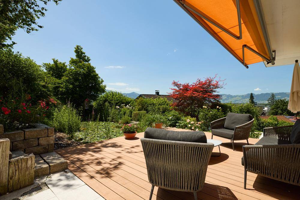 Große Holzterrasse mit modernen Gartenmöbeln, Markise und weitem Blick ins Grüne.