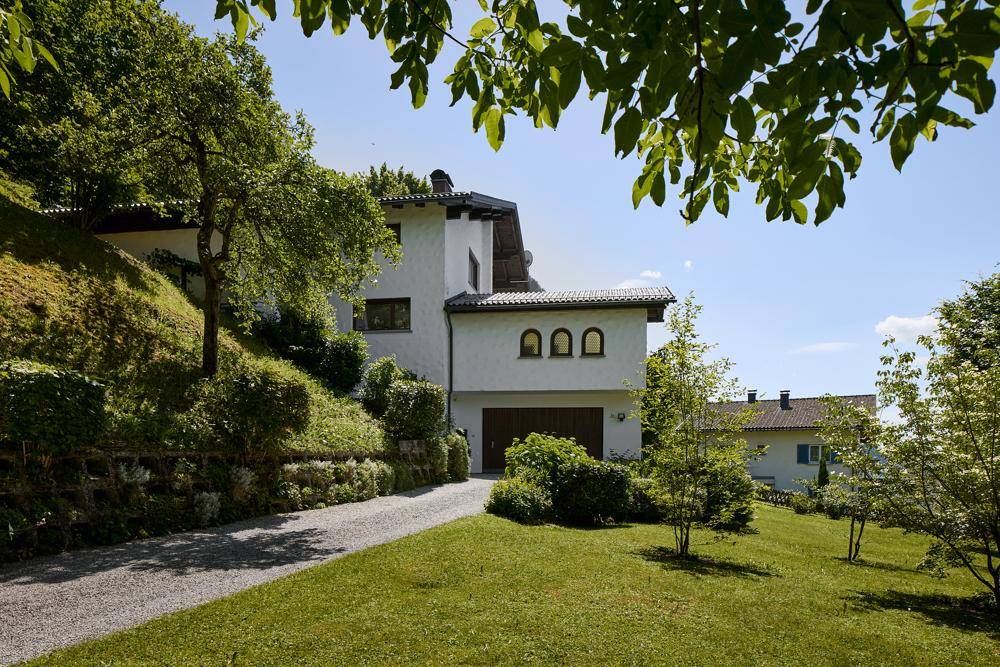 Zufahrt zum Haus mit Garage, umgeben von Rasenflächen und Bäumen.