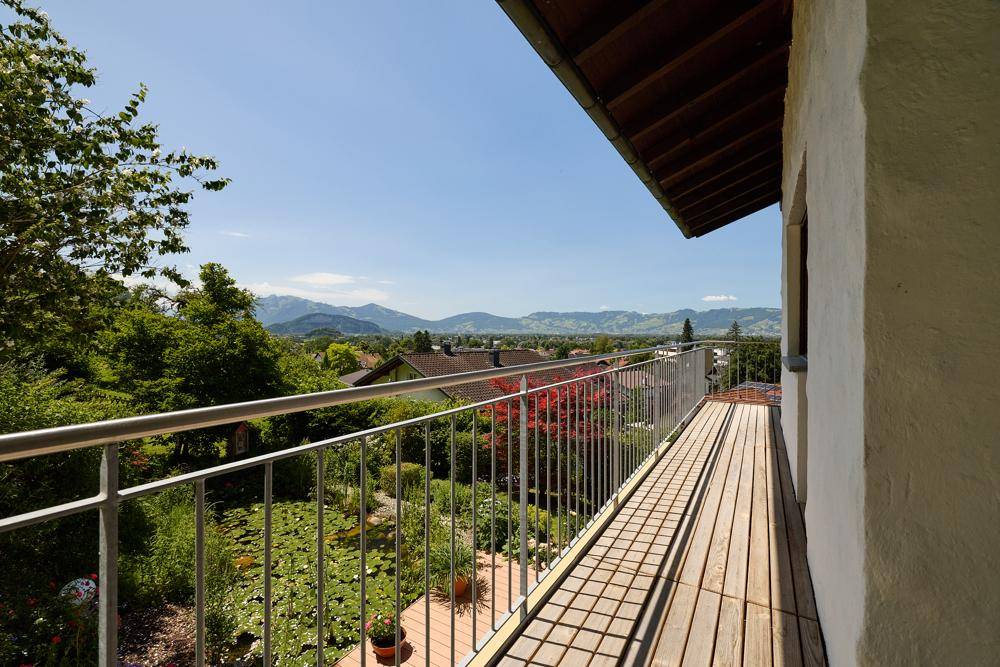 Langer Holzbalkon mit Metallgeländer und Panoramablick über die Landschaft und Berge.
