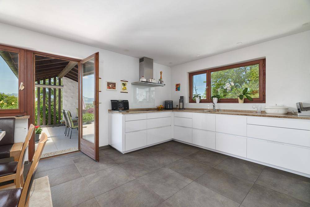 Moderne weiße Küche mit Fliesenboden, Granitarbeitsplatte und Zugang zur überdachten Terrasse.