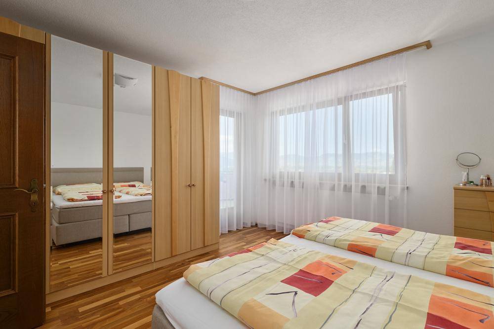 Gemütliches Schlafzimmer mit Holzparkett, Spiegelschränken und viel Tageslicht.