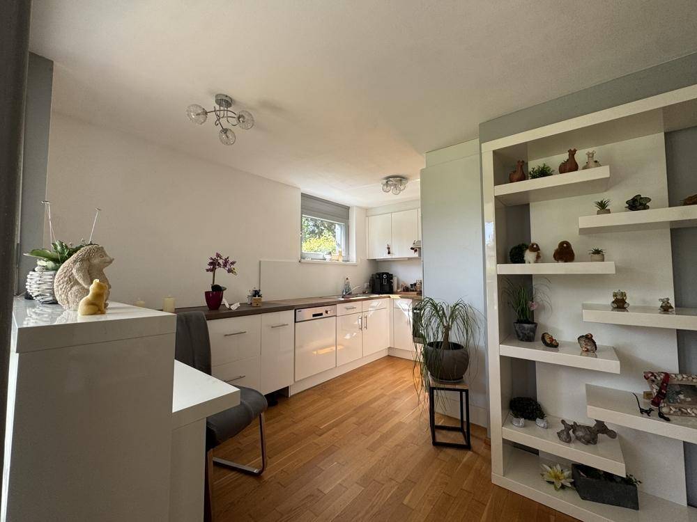Helle Küche mit weißen Schränken, Holz-Arbeitsplatte und einem Fenster, Teil eines offenen Wohnbereichs.