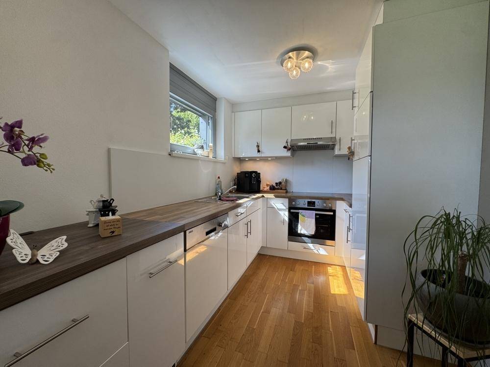 Moderne Einbauküche mit weißen Hochglanzfronten, Holz-Arbeitsplatte und integrierten Geräten.