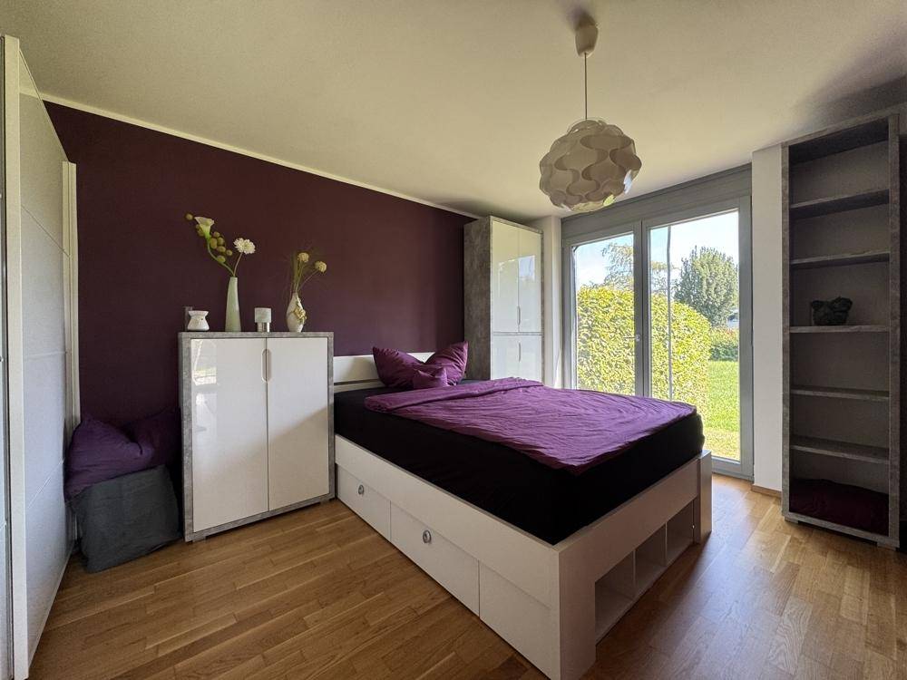 Gemütliches Schlafzimmer mit lila Akzentwand, Holzboden und direktem Zugang zum Gartenbereich.
