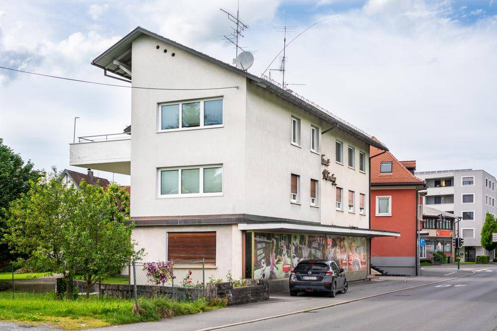 Mehrfamilienhaus an einer Straße mit schrägem Dach und mehreren Fenstern.