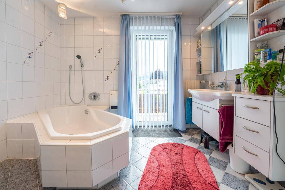 Helles Badezimmer mit Eckbadewanne, Duschvorrichtung und Balkonzugang.