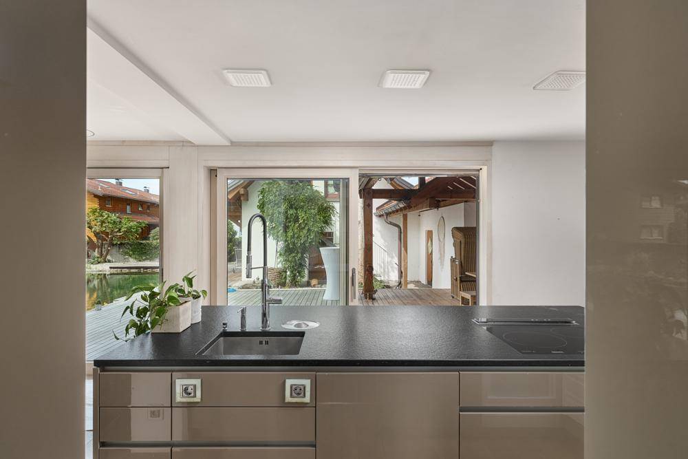 Moderne Küche mit dunkler Arbeitsplatte und Blick auf den Außenbereich mit Teich und Terrasse.