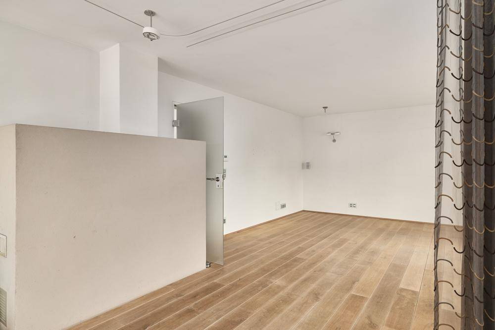 Heller Innenraum mit Holzfußboden und einer modernen Glastür, die zu einem weiteren Bereich führt.